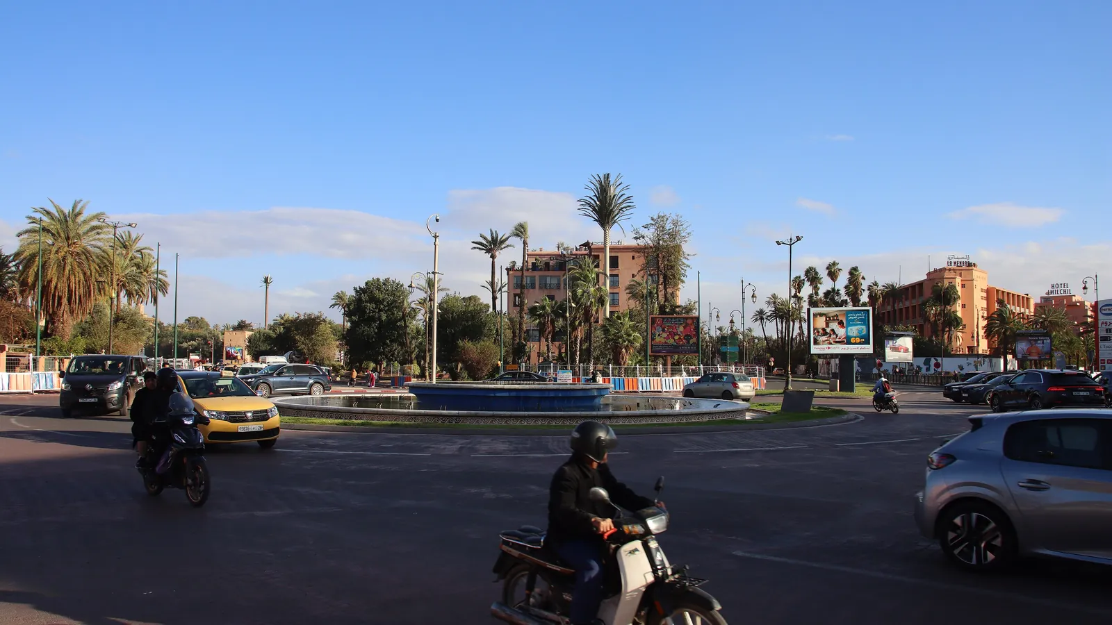 Rond-point de la place de la Liberté à Guéliz, palmiers, immeubles roses et scooters